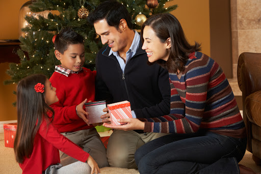 Family opening presents in front of Christmas tree &#8211; es