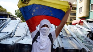 A demonstrator holds a Venezuelan flag in front of riot policemen – es