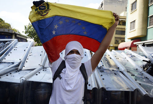 A demonstrator holds a Venezuelan flag in front of riot policemen &#8211; es