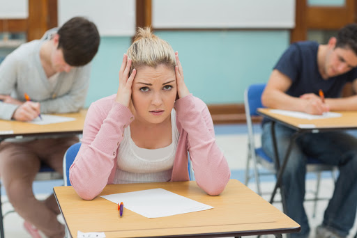 Student sitting at a table in a classroom while having an examination &#8211; es