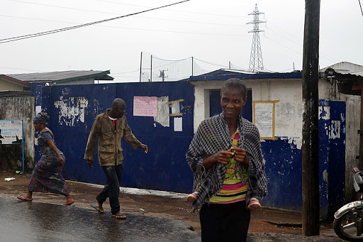 LIBERIA, Monrovia : People walk under the rain by a school that was used as an isolation ward for Ebola patients &#8211; es
