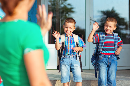 Two brothers waving back at their mother on their first day at school – es