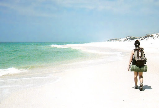 chica con mochila caminado a orillas del mar