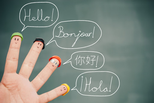 Four smiley fingers on a blackboard saying hello in English, French, Chinese and Spanish &#8211; es