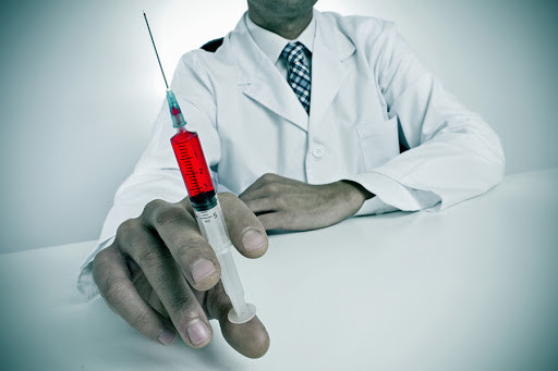 A doctor sitting in a desk holding a syringe &#8211; es