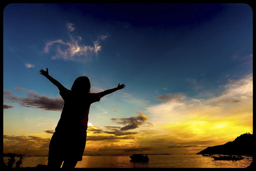 Silhouette of girl raising her hands to the sky at dusk © TaraPatta / Shutterstock &#8211; es