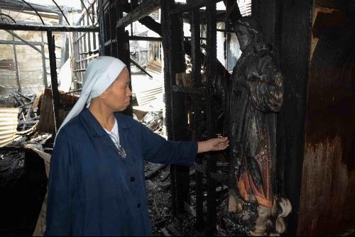 Religiosa inspecciona la imagen del sagrado Corazón de Jesús preservada de la destrucción del incendio.