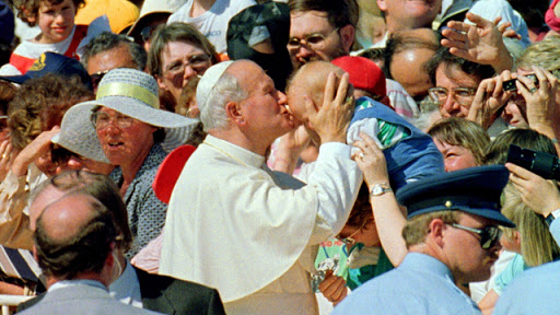 Pope John Paul II kisses a baby as he is welcomed to Australia in 1986. &#8211; es