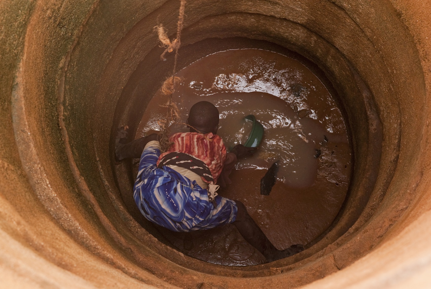 A Tanzanian teenager scoops up muddy water from a well.