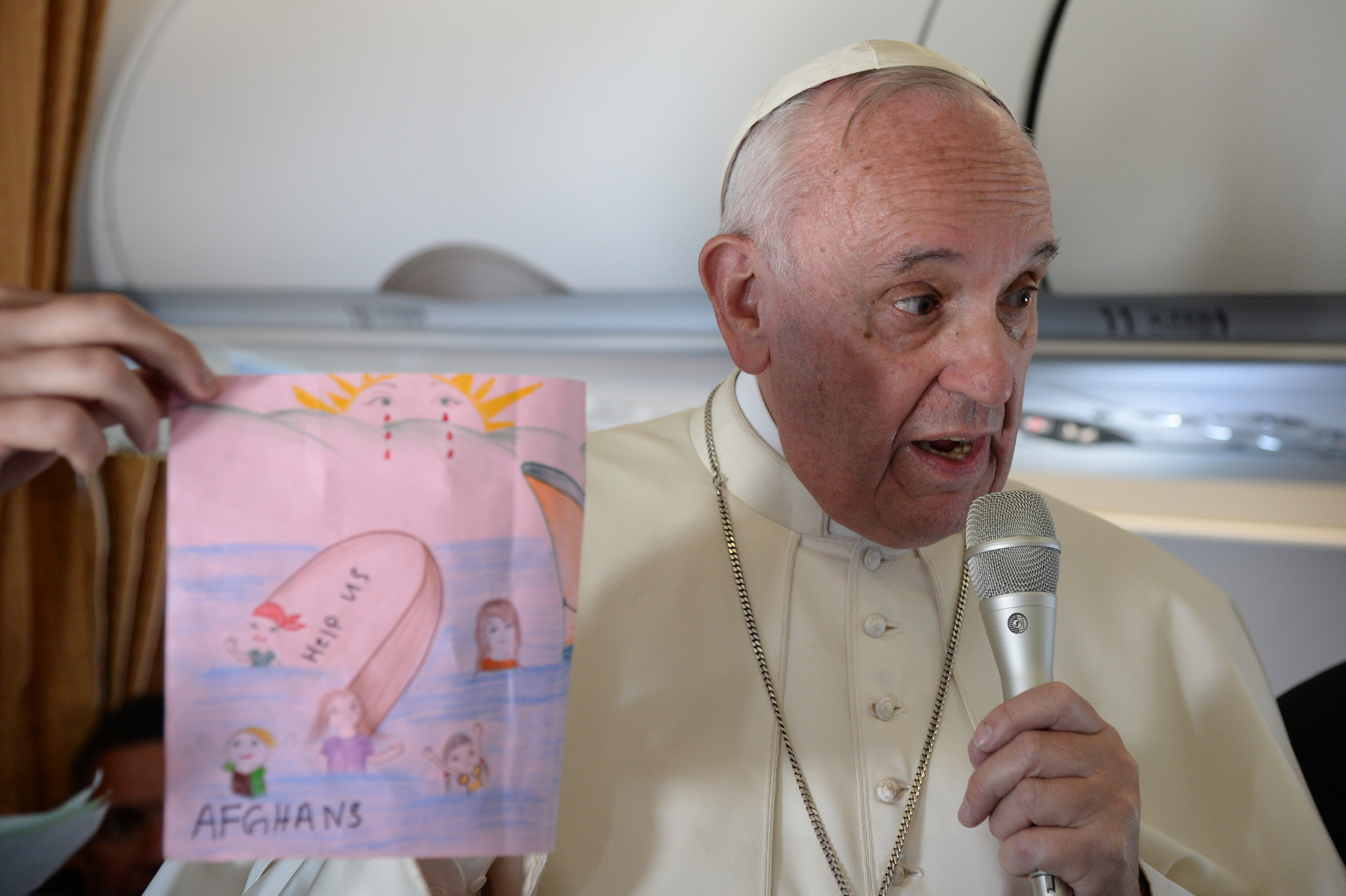 Pope Francis shows drawings made by children on his flight back to Rome following a visit at the Moria refugee camp on April 16, 2016 in the Greek island of Lesbos. Twelve Syrian refugees were accompanying Pope Francis on his return flight to Rome after his visit to Lesbos on Saturday and will be housed in the Vatican, the Holy See said. Pope Francis, Orthodox Patriarch Bartholomew and Archbishop of Athens and All Greece Ieronymos II visit Lesbos today to turn the spotlight on Europe's controversial deal with Turkey to end an unprecedented refugee crisis.  AFP PHOTO POOL / FILIPPO MONTEFORTE / AFP PHOTO / POOL / FILIPPO MONTEFORTE