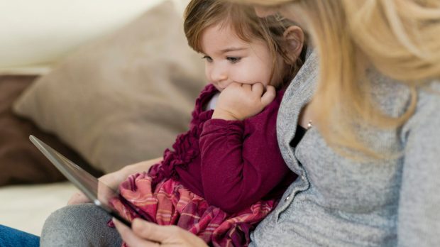 Little girl sitting on her mothers lap looking at digital tablet