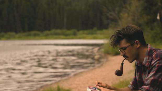 young man smokes pipe reads book river shore