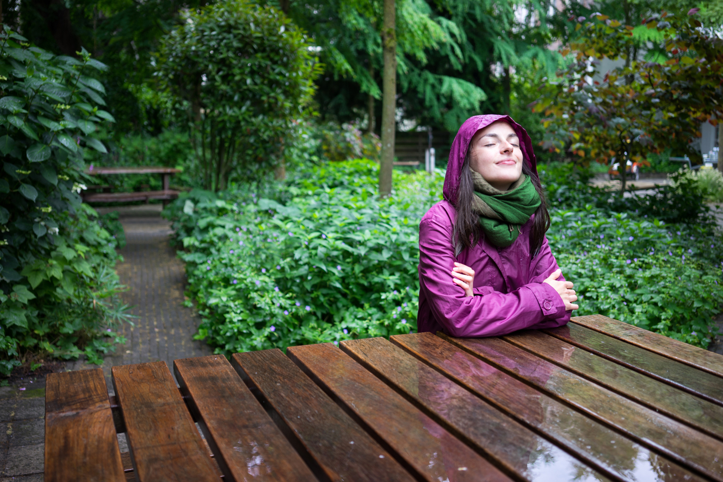 Beautiful young woman enjoying the rain in a garden decorated with eyes closed sits wooden table