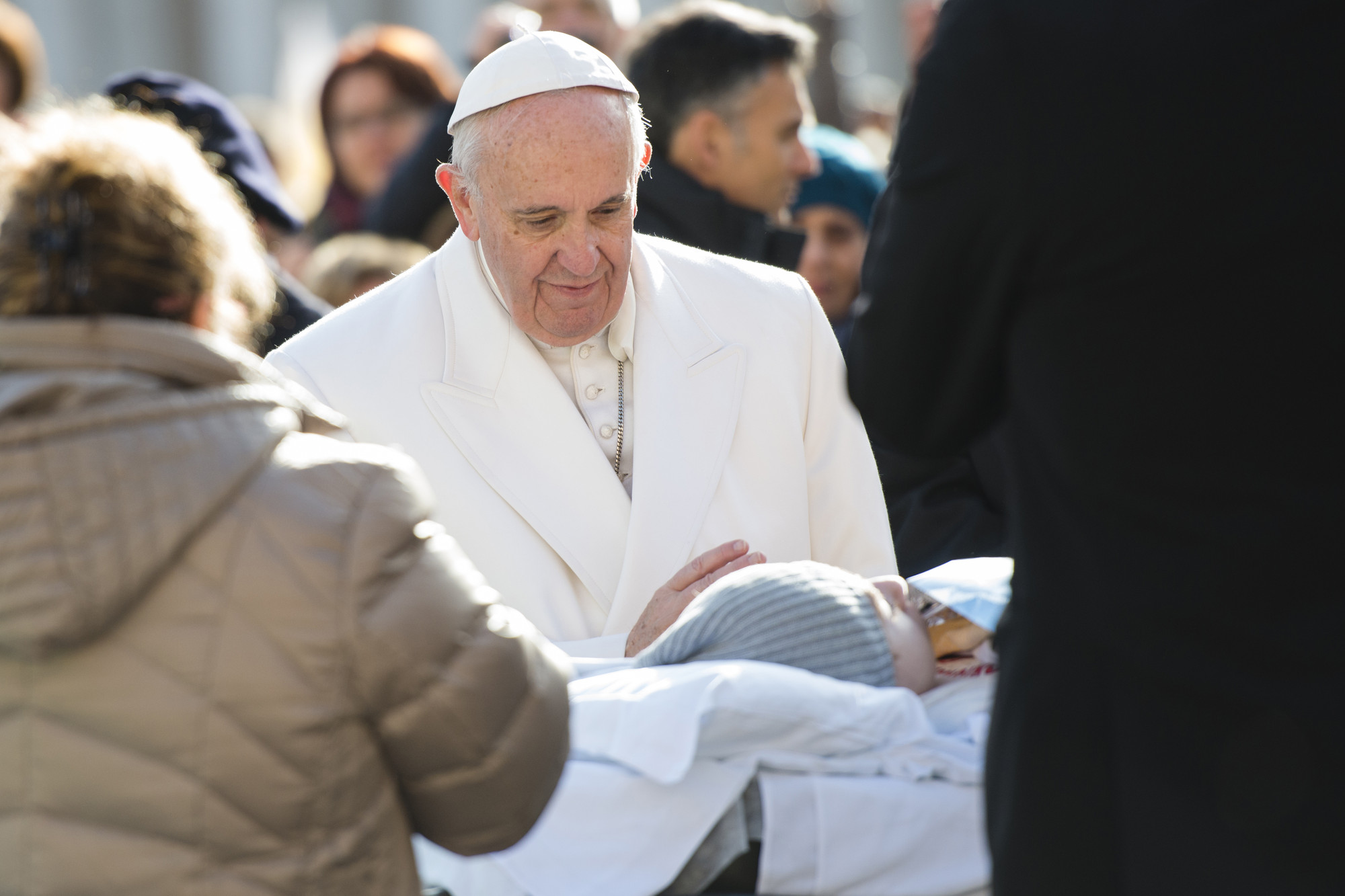 Pope Francis blesses a sick person lying on a bed