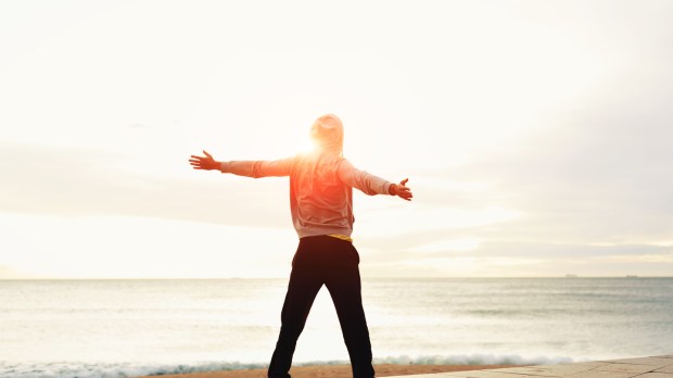 Freedom, relax and harmony in nature, Rear view of a young guy with his arms outstretched at the seaside standing next to the sea, happiness emotional concept