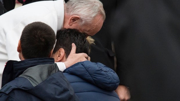 Pope Francis hugs two sick men.
