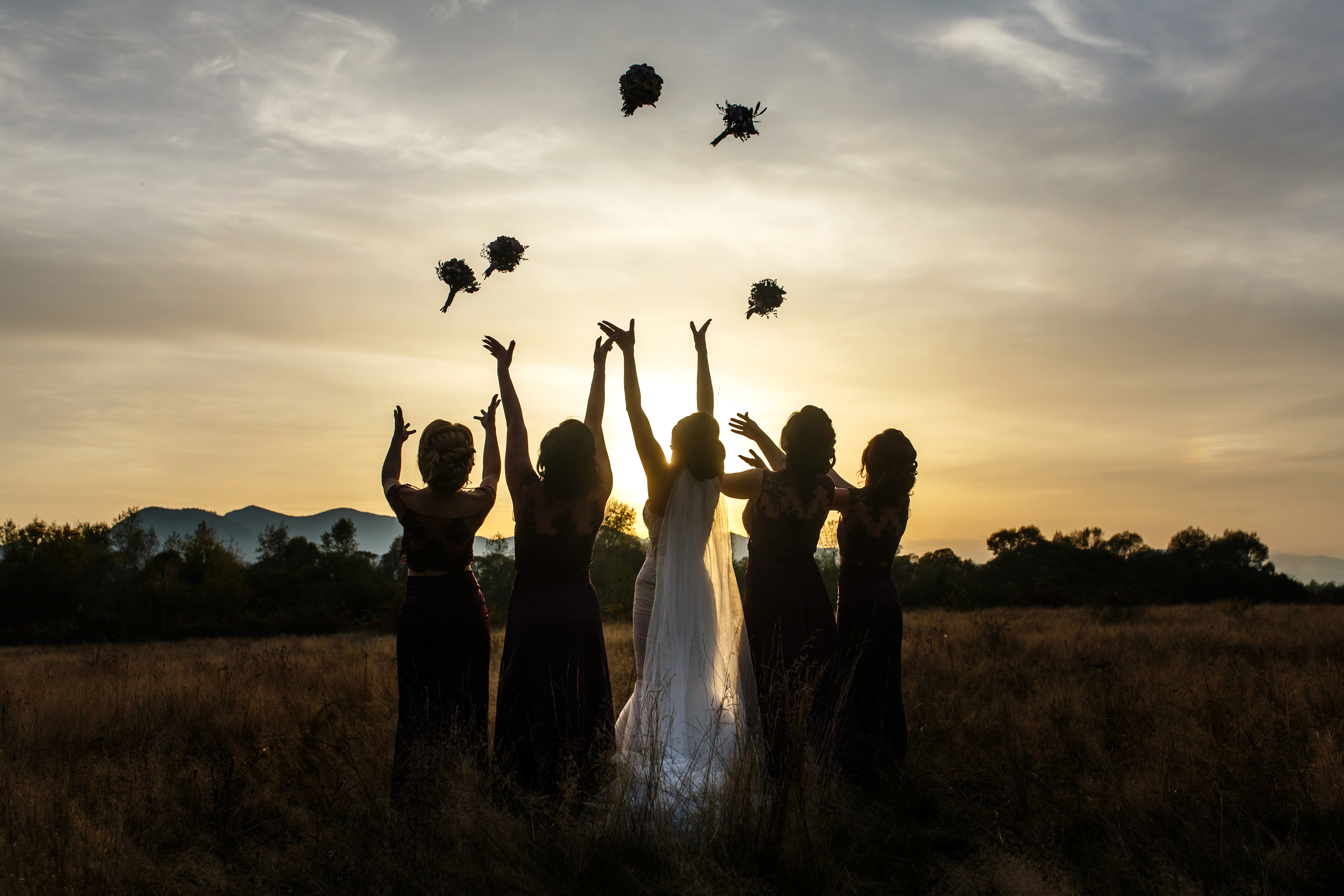 Bride and bridesmaids throw their bouquets up on evening field