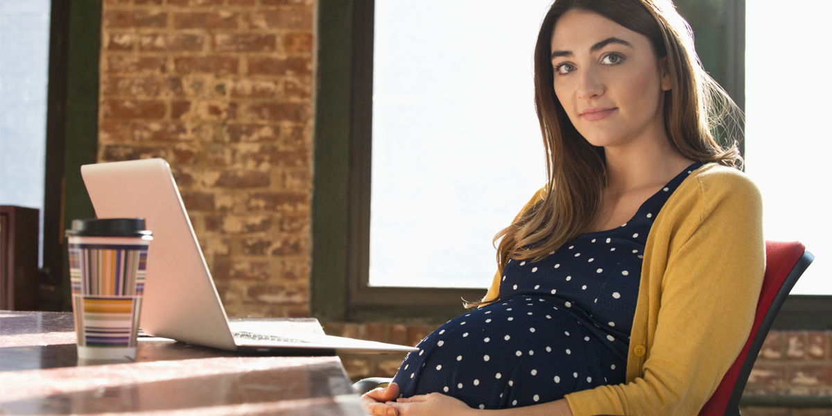 Młoda pracująca kobieta w ciąży siedzi w swoim biurze