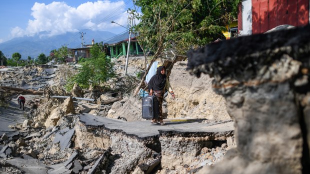 INDONESIA PALU / A woman with a suitcase makes her way along a destroyed road in Palu, Indonesia's Central Sulawesi on October 2, 2018, after an earthquake and tsunami hit the area on September 28. The bodies of dozens of students have been pulled from their landslide-swamped church in Sulawesi, officials said on October 2, as an international effort to help nearly 200,000 Indonesia quake-tsunami victims ground into gear. / AFP PHOTO / Jewel SAMAD