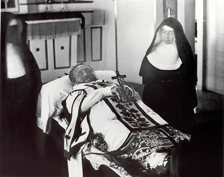 10_Father_Damien_on_his_funeral_bier_with_Mother_Marianne_Cope_by_his_side.jpeg
