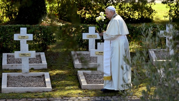 Pope Francis stands by graves with flowers at the French military cemetery