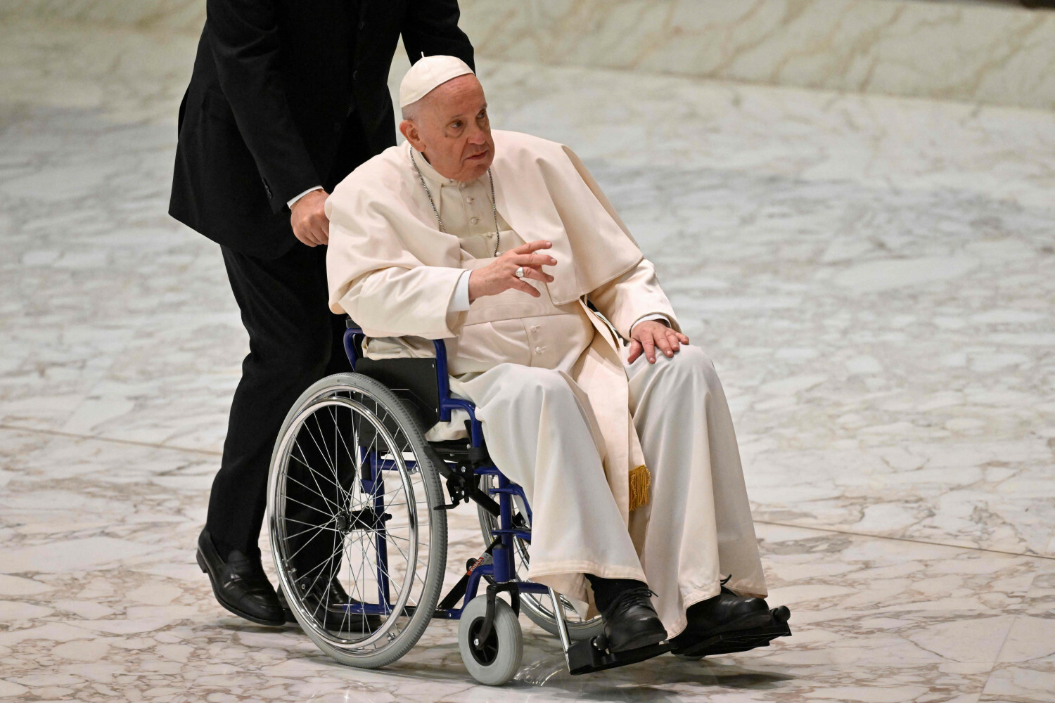 papież Franciszek jedzie na wózku inwalidzkim podczas audiencji w auli Pawła VI w Watykanie