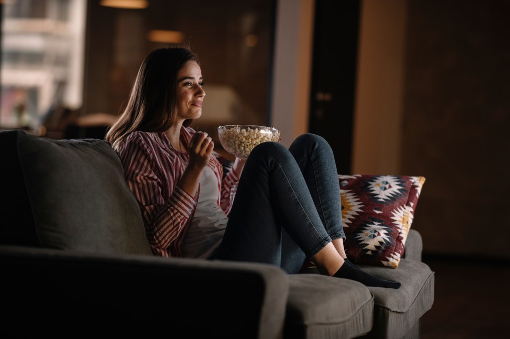Beautiful woman watching movie in the night sitting on a couch in the living room at home