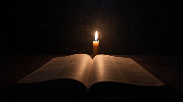 Biblia con vela encendida Bible and candle on a old oak wooden table. Beautiful gold background.Religion concept.