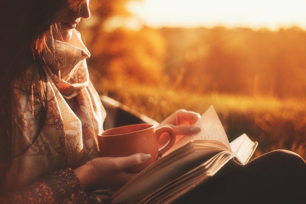 woman sits near a tree in an autumn forest and holds a book