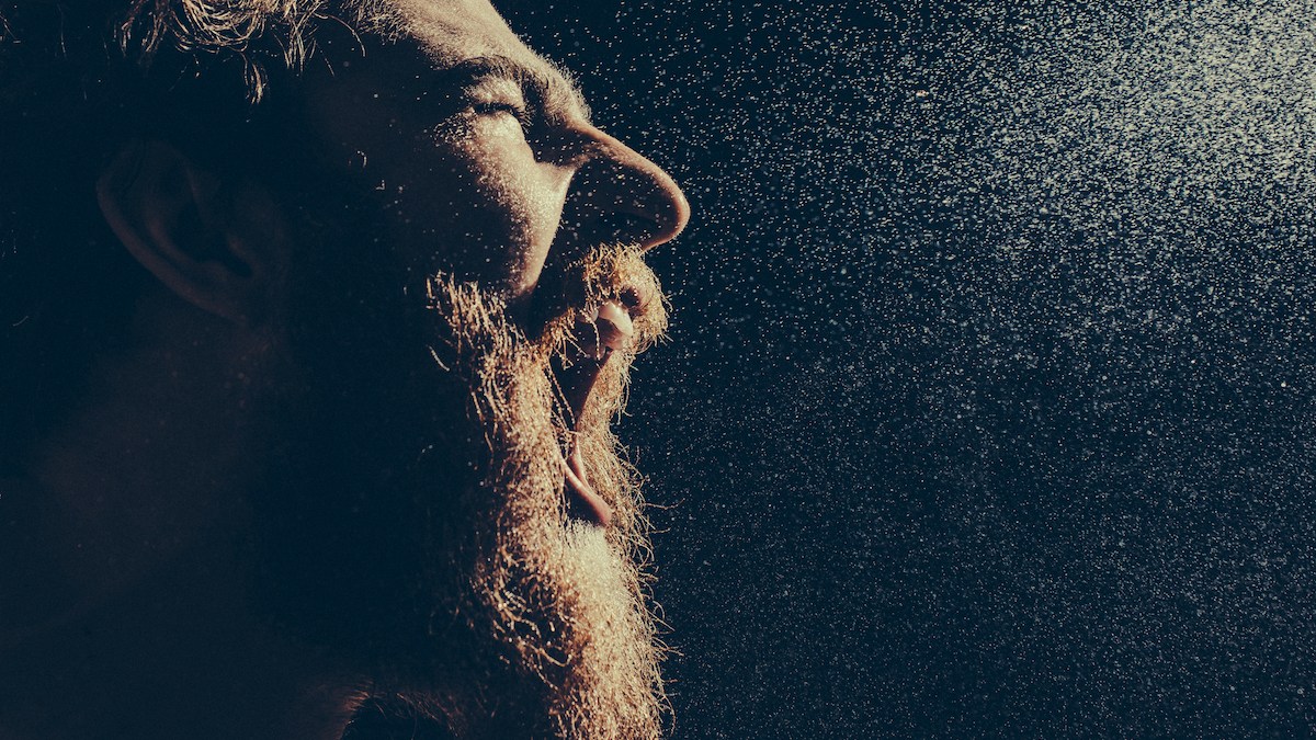Naked bearded man angrily screams into a spray of water against a black background with copy space