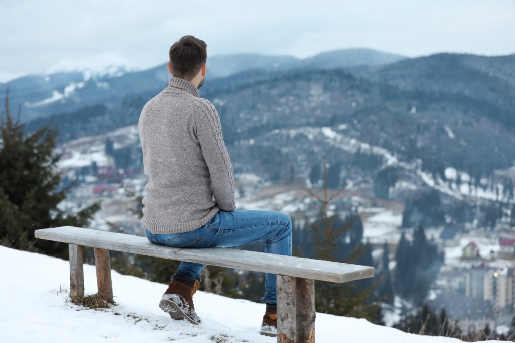 mężczyzna siedzi zimą na ławce i podziwia krajobraz pięknej górskiej doliny