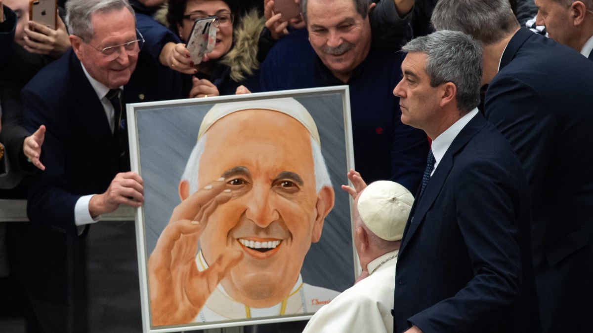 A visitor holds a portrait of Pope Francis as he passes