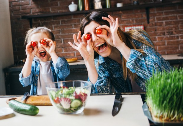 Matka wygłupia się z córką podczas wspólnego przyrządzania sałatki w kuchni