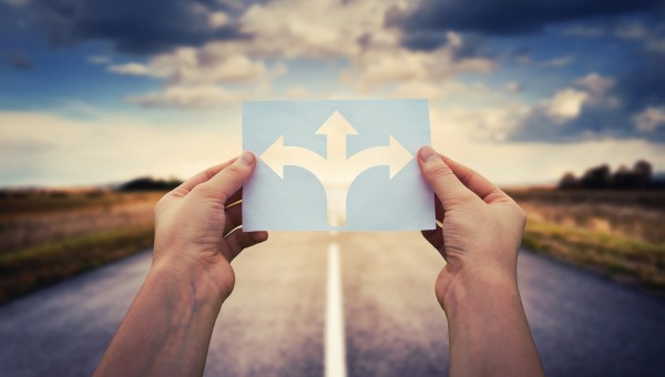 Manos sosteniendo papel con símbolo de cruce de flechas dividido en tres direcciones diferentes.