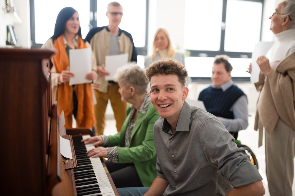 seniors with young man singing around piano at church