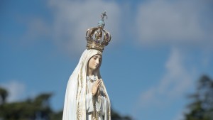 Estátua de Nossa Senhora de Fátima sob o céu azul com nuvens