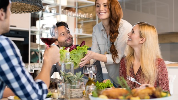 Smiling woman serving salads to her friends at home