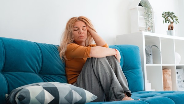 nieszczęśliwa kobieta siedzi na kanapie z podkurczonymi nogami