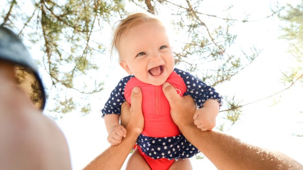 Ojciec podnosi malutkę córeczkę na rękach, a ona śmieje się radośnie