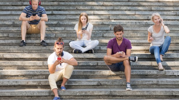 Pięcioro ludzi siedzi na dużych schodach w mieście i używa swoich telefonów