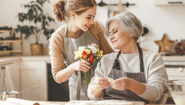 Dorosła córka wręcza swojej matce kwiaty podczas lepienia pierogów