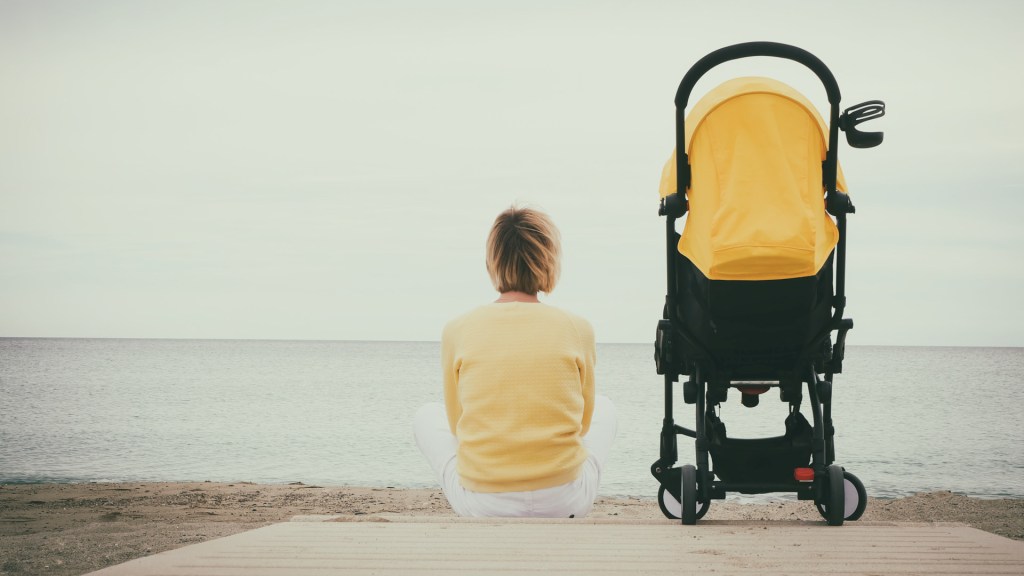 samotna matka siedzi na plaży obok wózka dziecięcego