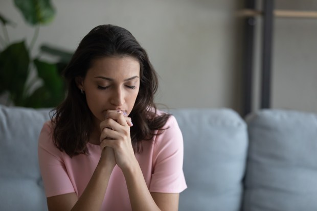 Preocupada joven mujer sentada en el sofá rezando a Dios