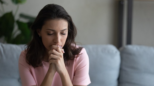 Preocupada joven mujer sentada en el sofá rezando a Dios