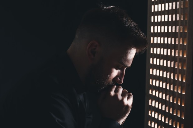 Joven sacerdote en cabina de confesión confesionario