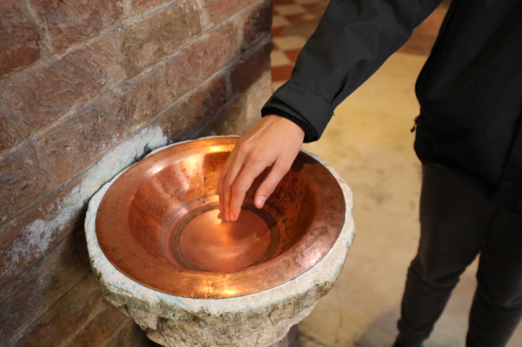 Faithful plunges his hand into the holy water of a Catholic church to make the sign of the cross