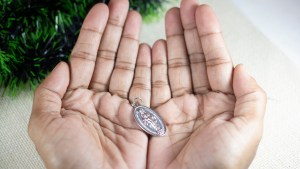 Girl-Hands-Holding-Miraculous-Medal-and-Praying-to-Our-Lady-Holy-Mary-Mother-of-God-shutterstock_1574