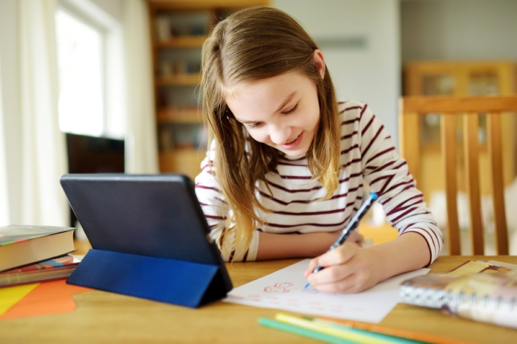 Preteen schoolgirl doing her homework with digital tablet at home