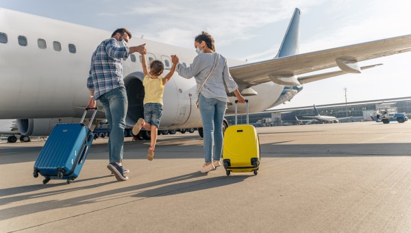 Back view of parents holding the hands of the child and going with suitcases to board the plane
