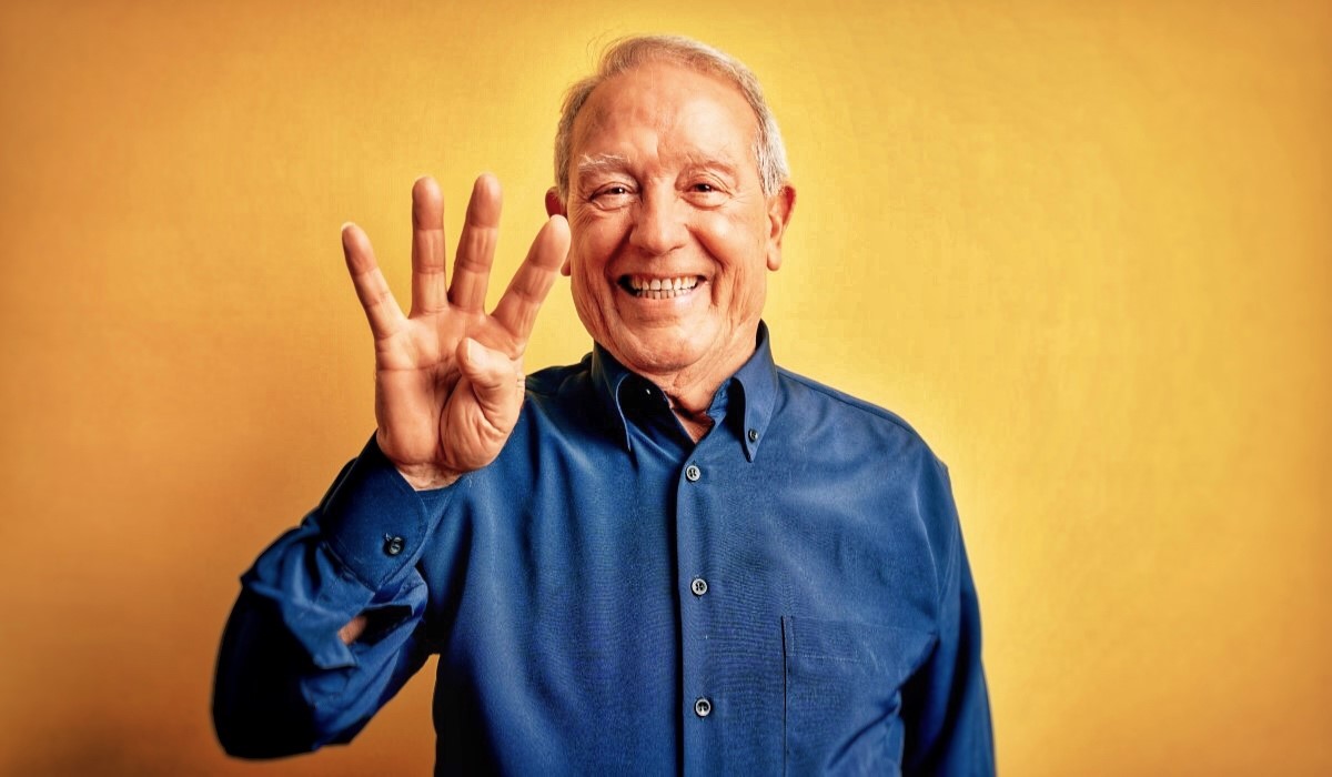 An elderly man holds up four fingers